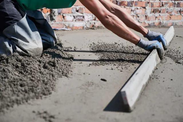 Stavebník vyrovnává vlhký beton na podlaze.