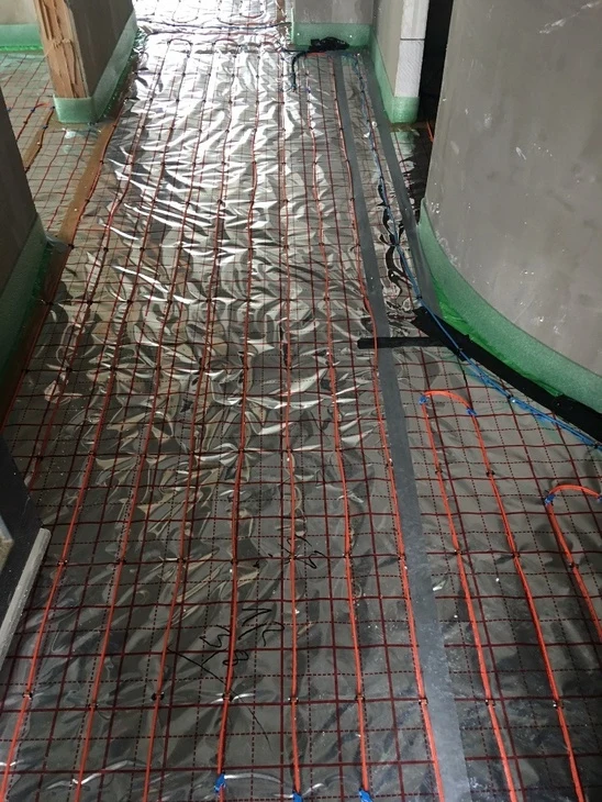 Montáž elektrického podlahového topení s kabely na izolační fólii.