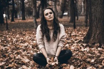 Žena sedí na podlaze listím v lese.