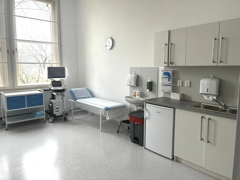 Vnitřek urologické ordinace s lůžkem a umyvadlem.