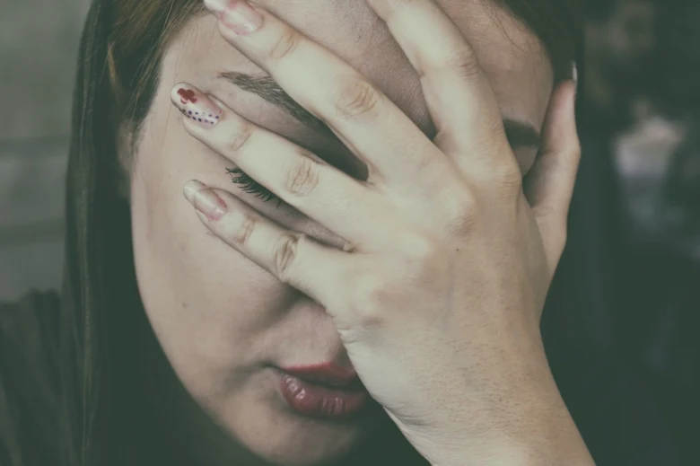 Žena zakrývá obličej rukou v důsledku nevolnosti.