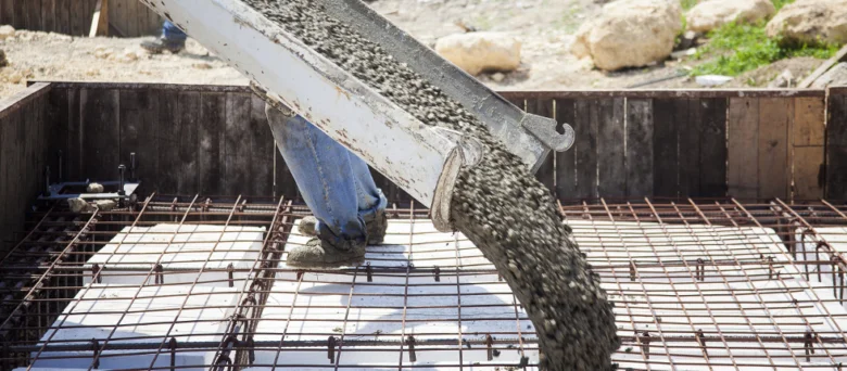 Pracovník nalévá beton do ocelové výztuže na stavbě.