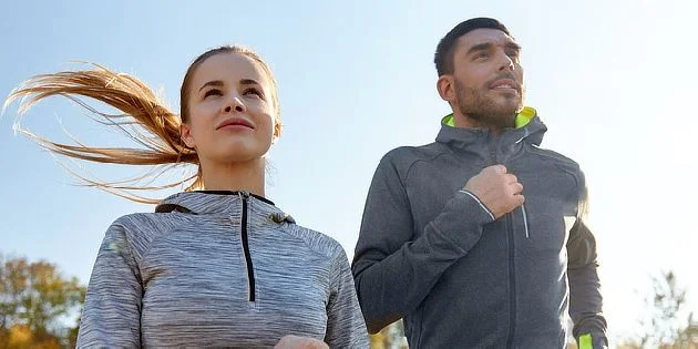 Muž a žena běží venku v sportovním oblečení.