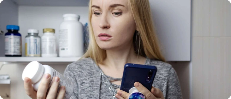 Žena v kuchyni s doplňky stravy hledá informace na mobilu.