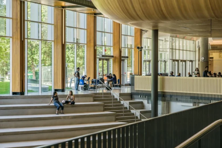 Studenti sedí na schodech v moderním univerzitním prostoru.