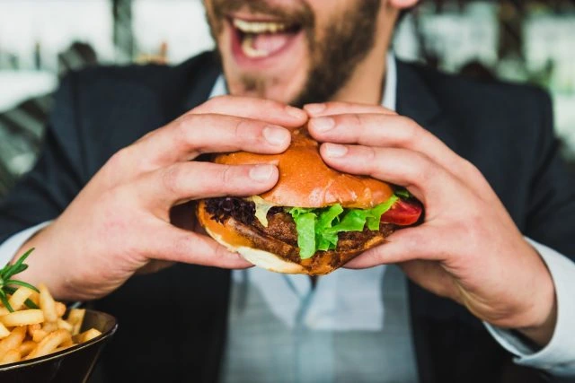 Muž v obleku drží velkou hamburgers s hranolky.