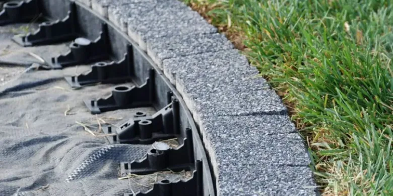 Křivá opěrná zeď z betonových bloků s drenážním systémem na trávníku.
