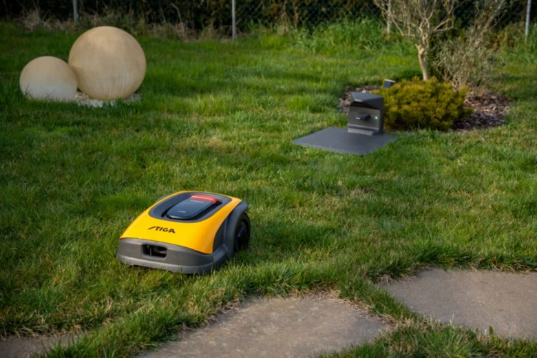 Žlutý robotický kosec pracuje na trávníku v zahradě.
