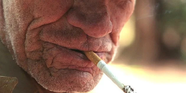 Starší muž kouří cigaretu s důrazem na ústní dutinu.