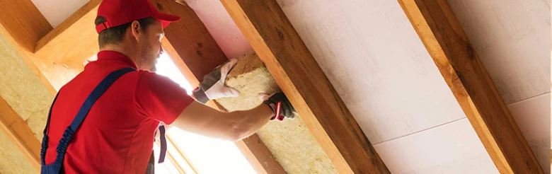 Muž zatepluje půdu v podkroví ručně izolačními materiály.