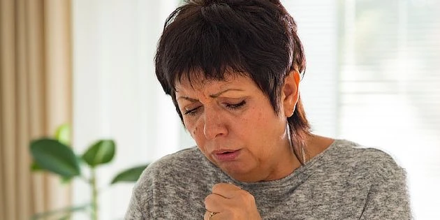 Žena kašle v interiéru s příznaky dýchacího potíže.