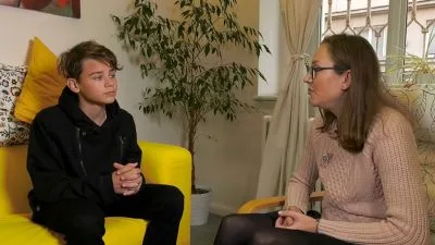 Muž sedí na žluté pohovce při rozhovoru s terapeutkou.