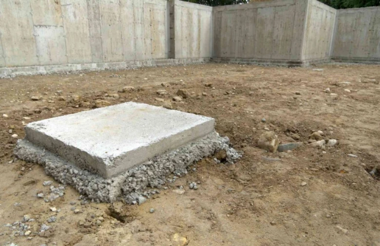 Čerstvě nalitý betonový patka na štěrkovém podkladu uvnitř stavebního objektu.