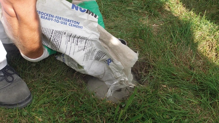 Lid nalévá suchý beton do díry v trávě.