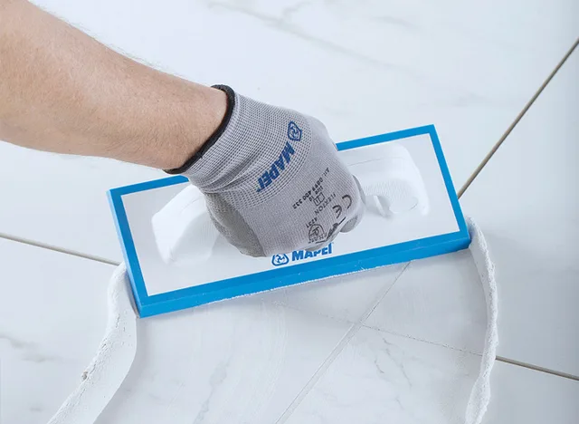 Ruka s rukavicí nanáší hydroizolační směs na dlažbu v koupelně.