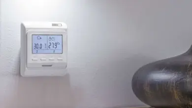 Bílý digitální termostat na zdi s displejem ukazující teplotu.
