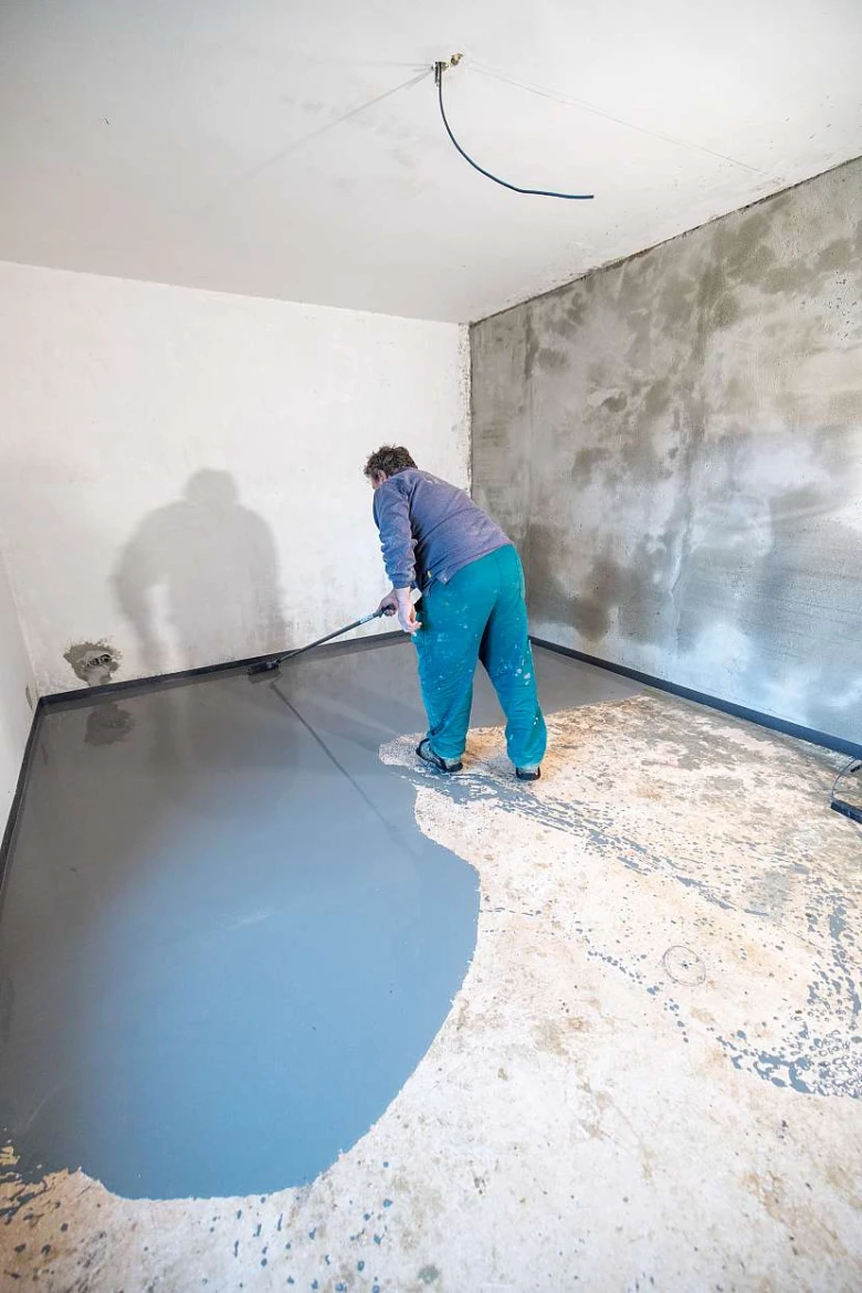 Pracovník nanáší epoxidovou podlahu válečkem na beton.