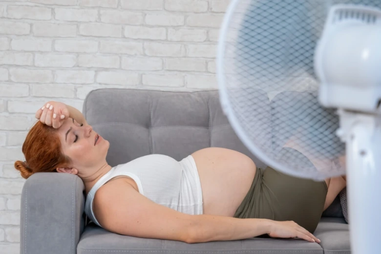 Těhotná žena leží na gauči s příznaky přehřátí v interiéru.