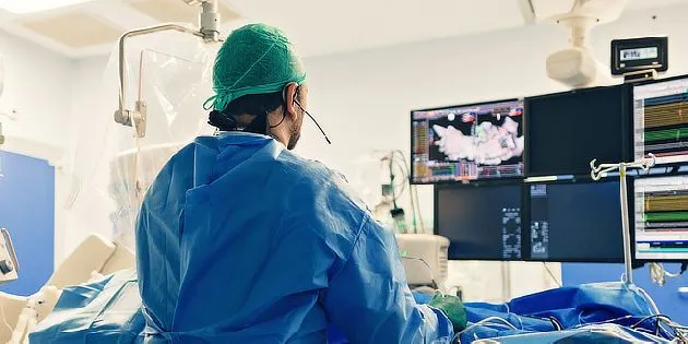 Chirurg v operační místnosti s monitory ukazujícími životní signály.