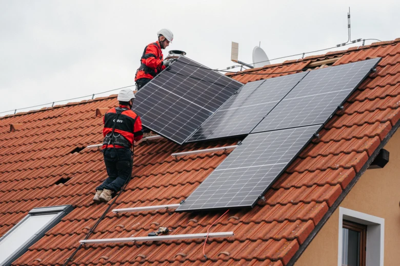 Dva dělníci montují fotovoltaické panely na střechu domu.