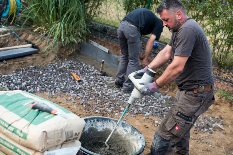 Muž míchá suchý beton v kbelíku na zahradě.