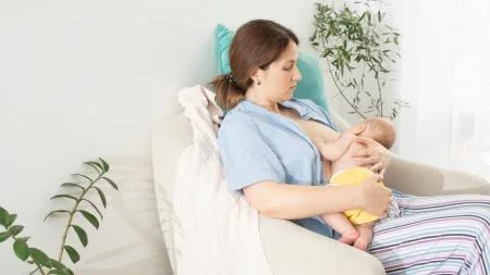 Matka kojí své dítě na pohovce v domácnosti.