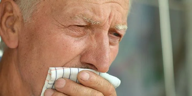 Starší muž utírá nos kapesníkem při léčbě rakoviny plic.