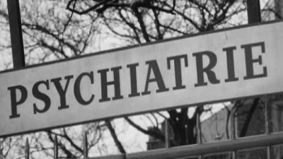 Bílá tabule s nápisem Psychiatrie na pozadí holých stromů.