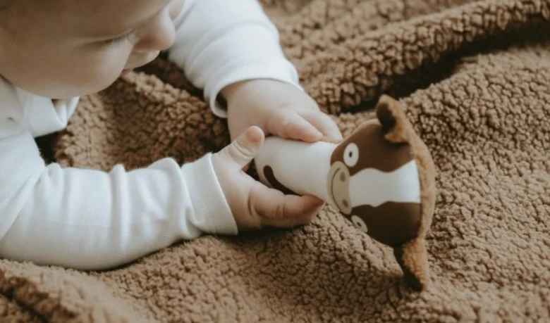Měsíček hraje s měkkou hračkou na hnědé dečce.
