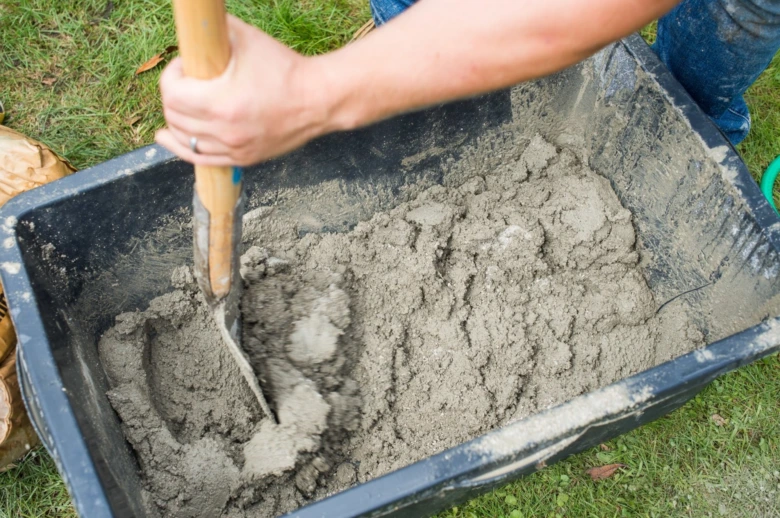 Ruce míchají beton lopatou v plastovém kontejneru venku.