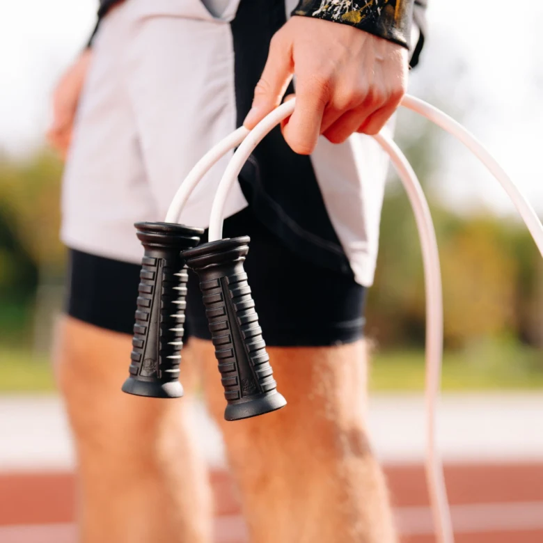 Sportovec drží švihadlo před nohama na běžecké dráze.