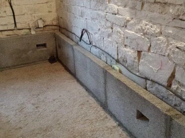 Nově nalitý betonový sokl v nezařízené místnosti s cihlovými zdmi.