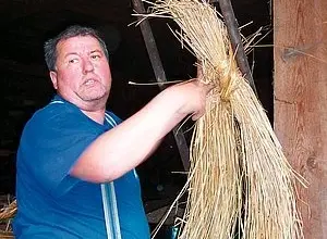 Muž drží svazek slámy pro doškovou střechu v stodole.