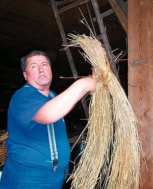 Muž drží svazek slámy pro doškovou střechu v stodole.