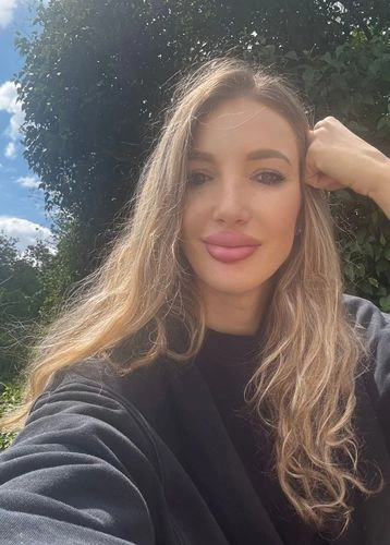 Žena s dlouhými blond vlasy se fotí venku.