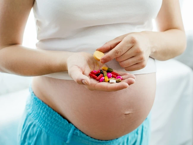 Těhotná žena drží v dlani různé vitamíny a doplňky stravy.